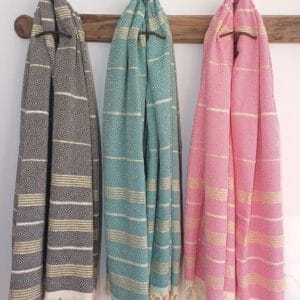 3 Toallas de playa en varios colores, con rayas crudas y doradas en un perchero de pared