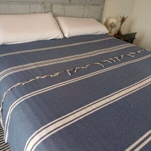 Cama cubierta con una colcha de color azul grisáceo y rayas blancas.