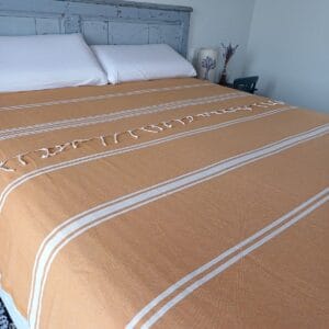 Cama cubierta con una colcha de color curry y rayas blancas.