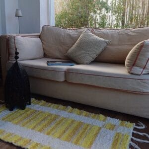 alfombra amarillo con rayas blancas delante de un sofá beige, faroles marroquíes en el suelo