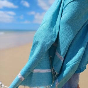 Mujer en la playa envuelta en una toalla Fouta playa Bohemia turquesa.