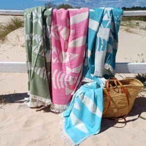 4 colores de Foutas Playa XL colocadas sobre una barrera y en una cesta cerca de la playa.
