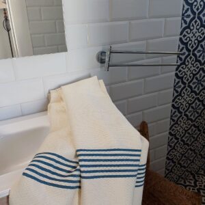 Toalla de baño beige con rayas azul petróleo sobre un lavabo.